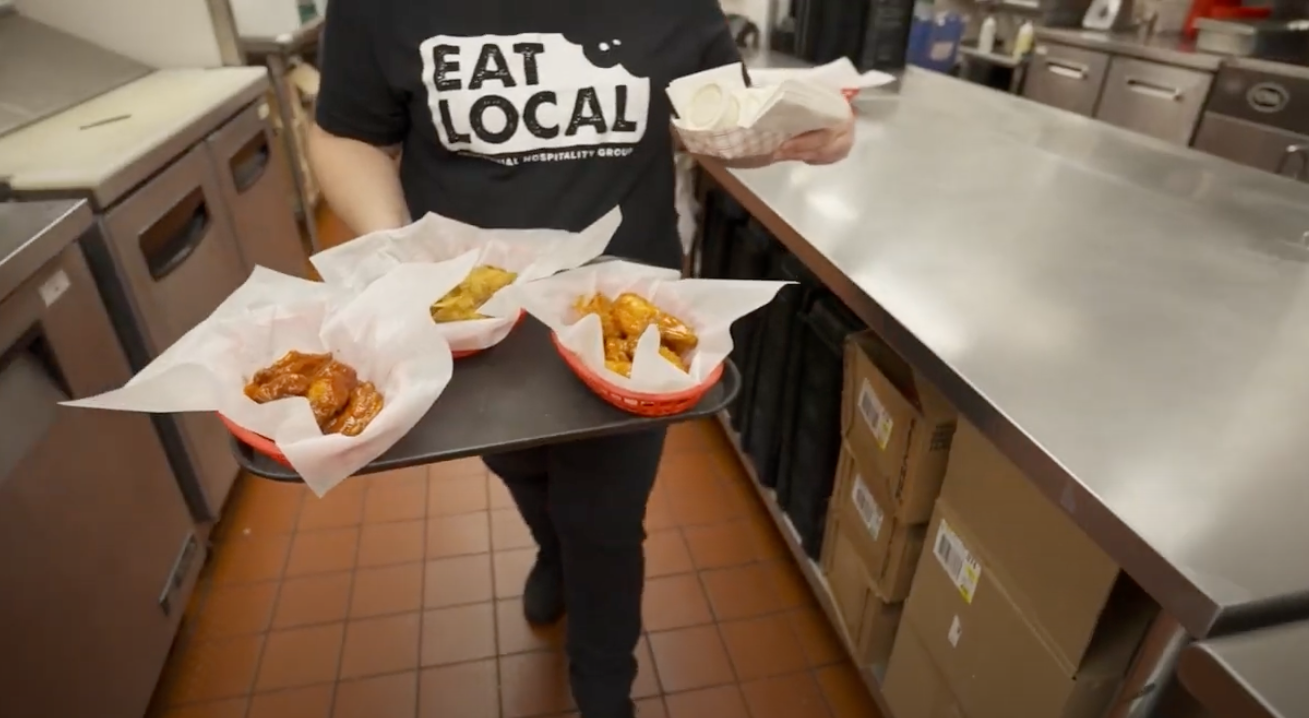 General manager walks baskets of chicken wings through the kitchen